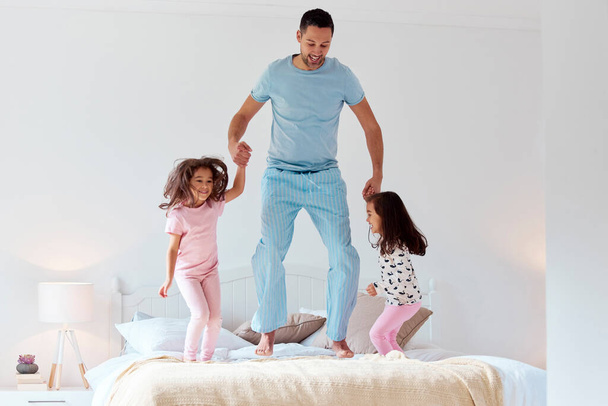 Youre the fun parent, just dont tell Mom. a man jumping on a bed with his two daughters - Foto, Bild