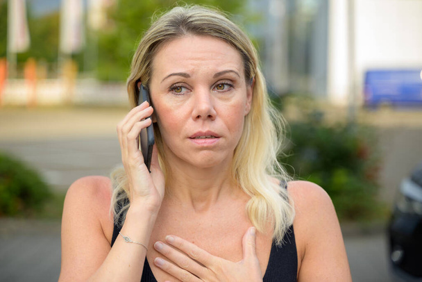 Woman looking stressed as she listens to a call on her mobile phone outdoors on a town street - Photo, Image