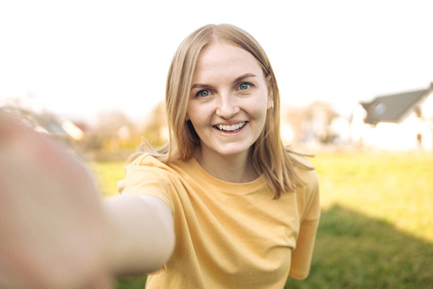 Excited happy young woman enjoys free time and walking in city park, make selfie by camera poses has fun - Fotó, kép