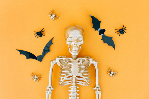 Halloween composition with spiders, bats and golden skeleton over orange background. Halloween party invitation template - Fotografie, Obrázek