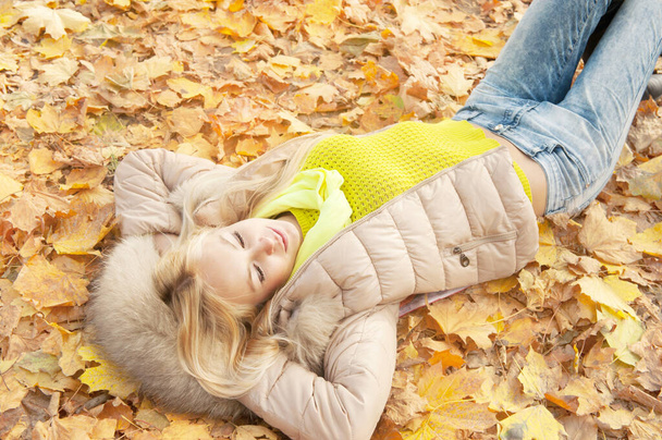 Smiling happy young blonde woman laying in autumn leaves, top view, healthy lifestyle concept, outdoor in autumn park - Zdjęcie, obraz
