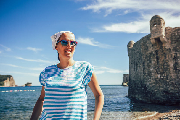Зріла жінка в шарфі на голові, що йде уздовж узбережжя набережної старого туристичного міста
 - Фото, зображення