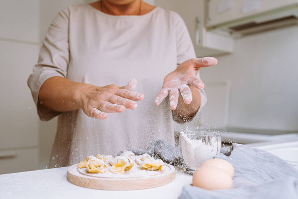 Chef's hands spray flour on dough products. Dumplings, handmade tortellini in home kitchen. Chef woman housewife in home clothes sprays flour on dough - Fotoğraf, Görsel