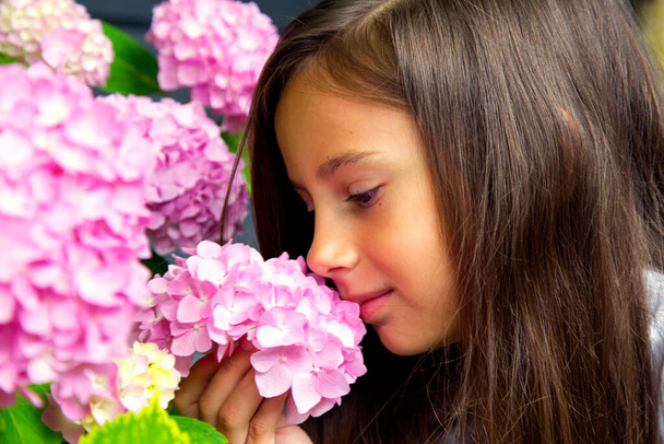 Portrait of a little beautiful girl with a bouquet of hydrangeas in her hands. Child girl smells hydrangea flowers. The concept of childhood, happiness, carelessness and nature.  - Photo, image