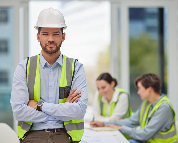 I trust my team completely. Cropped portrait of a handsome young male construction worker standing with his arms folded with his colleagues in the background - 写真・画像