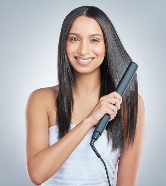 I prefer wearing my hair straight. an attractive young woman standing alone and using a hair straightener to straighten her hair in the studio - Φωτογραφία, εικόνα