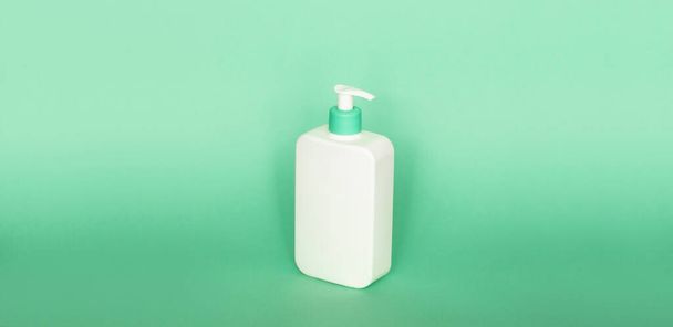 White plastic soap dispenser pump bottle isolated on green background. Skin care lotion. Bathing essential product. Shampoo bottle. Bath and body lotion. Fine liquid hand wash. Bathroom accessories - Photo, Image