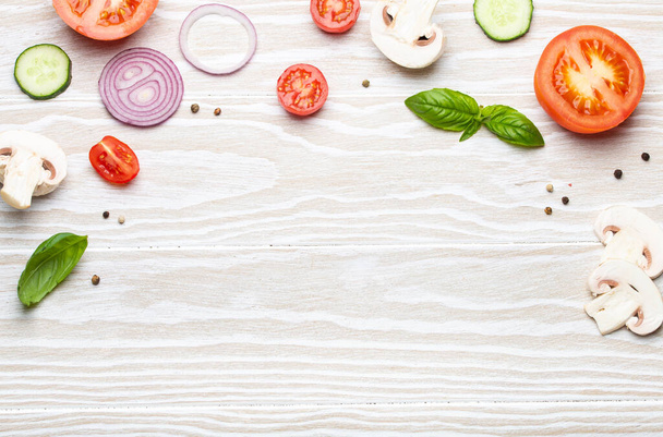 Food cooking background: arranged fresh ingredients, basil, cherry tomatoes, mushrooms, cut cucumber, onion, chilli pepper, spices on white wooden background top view, space for text - Фото, изображение