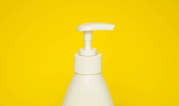 White plastic soap or shampoo dispenser pump bottle isolated on yellow background. Skin care lotion. Bathing essential product. Shampoo bottle. Bath and body lotion. Fine liquid hand wash - Foto, Imagem