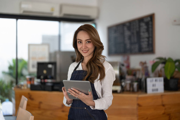 Attractive young beautiful asian barista with apron using digital tablet in coffee shop - Fotografie, Obrázek