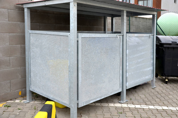 yard for placing containers for sorting household waste. gray door and halving of perforated metal grid, expanded metal. stone wire baskets filled and sunk into grassy slope. reclining place - Foto, Imagem