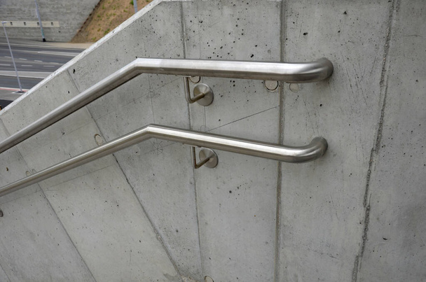 a staircase with concrete sides at a public building. the safe staircase has two handrails, one with a reduced height for children under 12 at the entrance to the school - 写真・画像