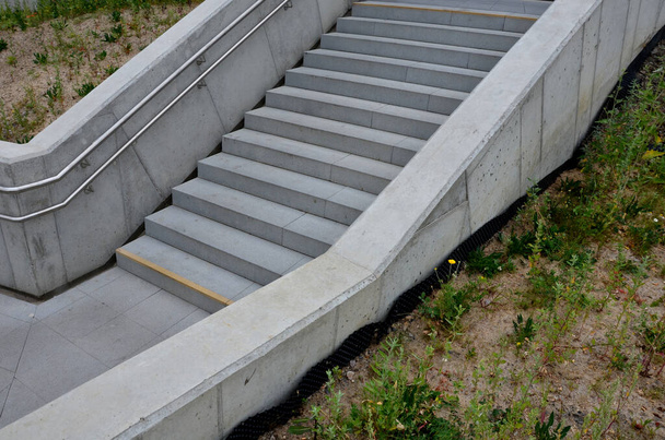 a staircase with concrete sides at a public building. the safe staircase has two handrails, one with a reduced height for children under 12 at the entrance to the school - Фото, изображение