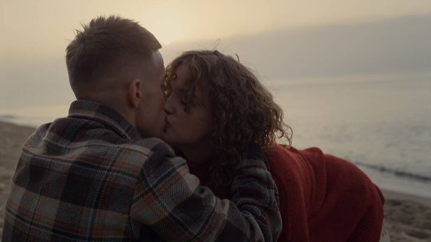 Romantisches Paar küsst sich am Strand bei Sonnenaufgang. Sinnliche Mädchen und Kerl umarmen einander. Verspielte Frau flirtet beim Date mit Mann. Freund und Freundin genießen die Freizeit auf See. Zärtlichkeit - Foto, Bild