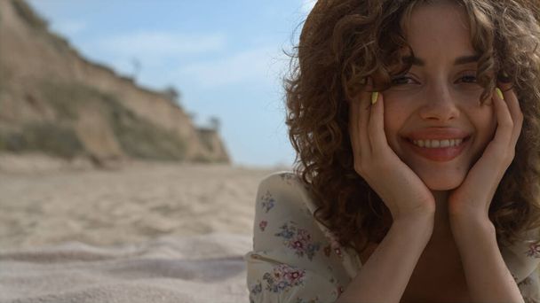 Portrait of cheerful attractive woman wearing straw hat in front beautiful seashore. Curly pretty lady smiling camera feeling happy on nature. Young carefree girl tourist lying beach sand close up. - Fotografie, Obrázek