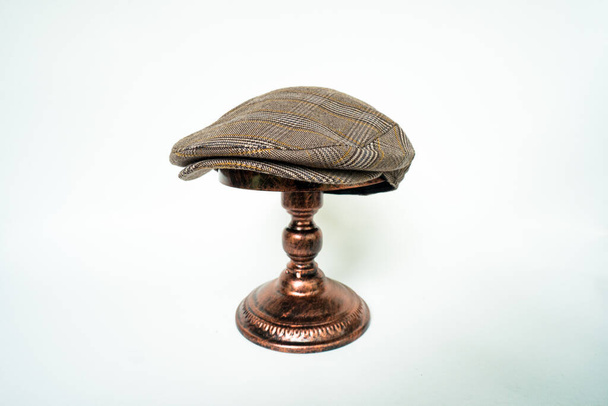 Деталь скаліченої шапки або плоскої шапки в темно-коричневому візерунку оселедець тканина, встановлена на бронзовій голові манекен на білому тлі
 - Фото, зображення