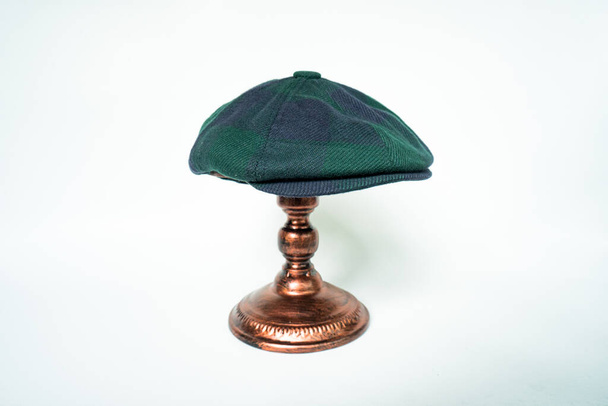 Detail of a classic eight-panel newsboy hat, in dark green pattern herringbone tweed fabric set against a bronze head mannequin on a white background - Foto, immagini