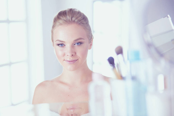 Young woman in bathrobe looking in bathroom mirror. - 写真・画像