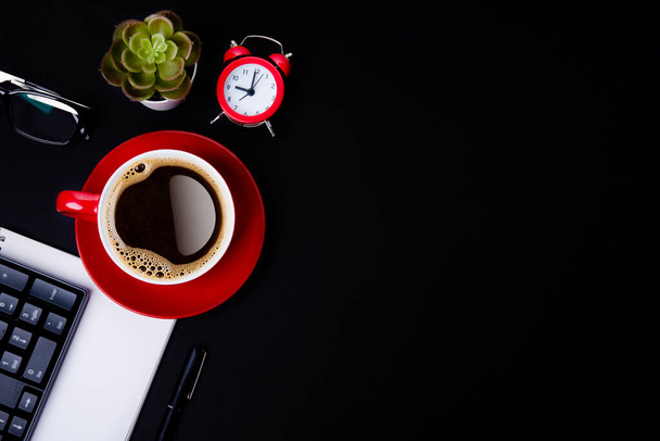 červený šálek kávy, pera, brýle, alarm, rostlina, telefon a papír na černém pozadí jako pracoviště horní pohled prostor pro text - Fotografie, Obrázek