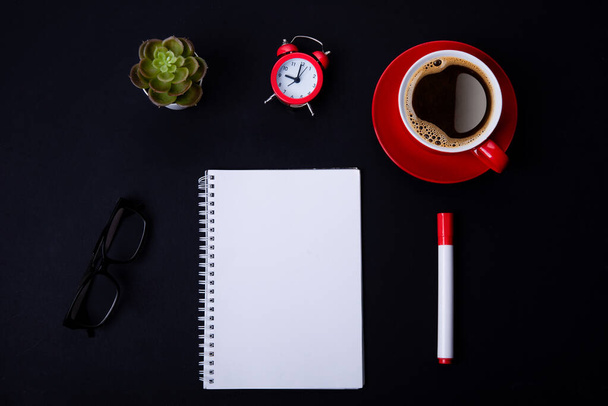 red cup of coffee, pen, glasses, alarm,  plant, phone, and paper on a black background  as workplace top view space for text - Φωτογραφία, εικόνα