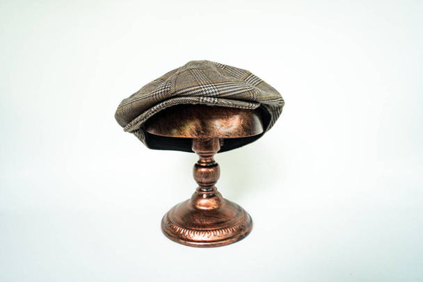 Detail of a classic eight-panel newsboy hat, in dark brown herringbone tweed fabric set against a bronze head mannequin on a white background - Foto, Imagen