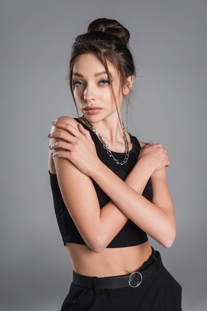 trendy woman with makeup and silver necklace posing with crossed arms isolated on grey - Foto, afbeelding