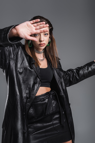 young woman in fashionable leather clothes gesturing near camera on blurred foreground isolated on grey - Foto, immagini