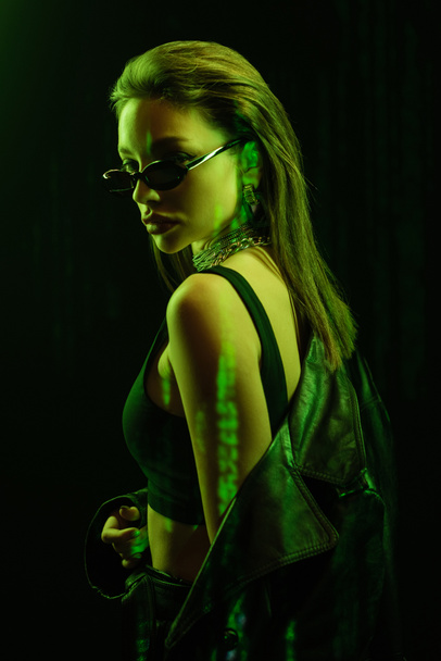 молода жінка в верхній частині культури і модні сонцезахисні окуляри в зеленому світлі ізольовані на чорному
 - Фото, зображення