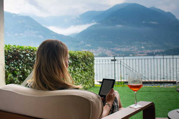 Female Relaxing and Drinking Aperol Spritz in chair infront of Lake Como in Italy - Foto, Imagen