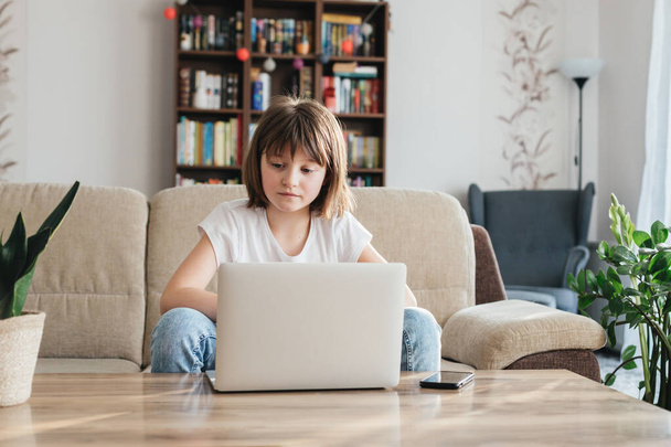 Девочка учится дома с помощью ноутбука. Ребенок смотрит вебинар или готовится к экзамену онлайн. Дистанционное обучение детей. - Фото, изображение