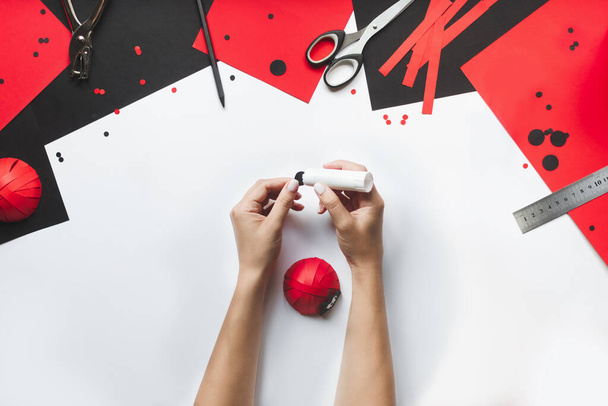 How to make paper red and black ladybug toy with children at home. Step by step instructions. Hands making DIY summer project. Top view. Step 11. Glue dots and the ladybugs face.  - Foto, afbeelding