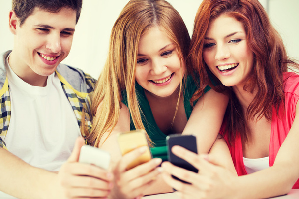 three smiling students with smartphone at school - Zdjęcie, obraz