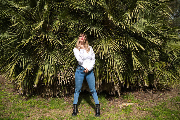 Pretty, blonde, young woman having fun making different expressions in front of green palm trees in the park. Holiday and leisure time concept. Various expressions. - Фото, изображение