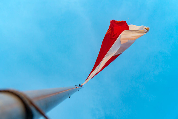 This red and white flag is the national flag of the Indonesian state which is flying in a clear blue sky with clumps of clouds around it - Fotó, kép