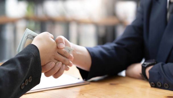 An Asian female lawyer or business legal consultant at the office desk receives money and shaking hand with her male client. cropped imag - Photo, Image