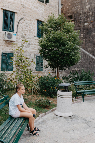 Girl Tourist Resting in the Ancient Narrow Street On A Beautiful Summer Day In MEDITERRANEAN MEDIEVAL CITY, OLD TOWN KOTOR, MONTENEGRO. Young Beautiful Cheerful Woman Walking On Old Street - 写真・画像