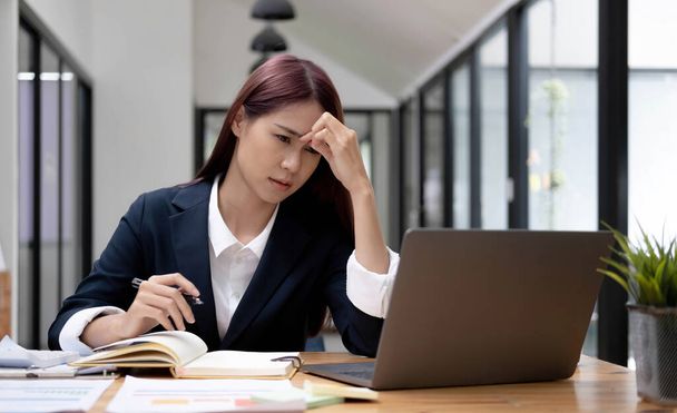 Jeune femme asiatique se sentant migraine souche de la tête. Fatiguée, femme d'affaires surmenée financière tout en travaillant sur ordinateur portable dans le bureau - Photo, image