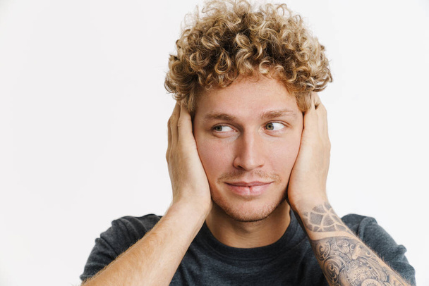 Young blonde man with curly hair smiling and covering his ears isolated over white wall - Fotoğraf, Görsel