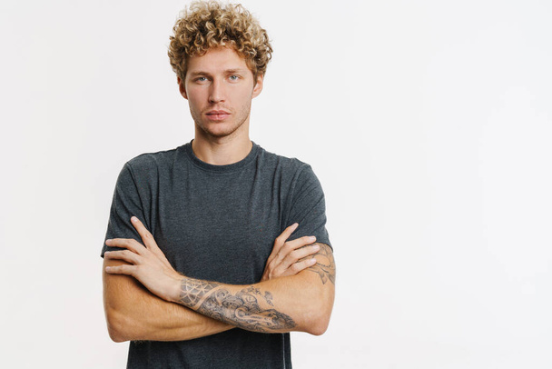 Young blonde man looking at camera while posing with arms crossed isolated over white wall - Foto, Bild