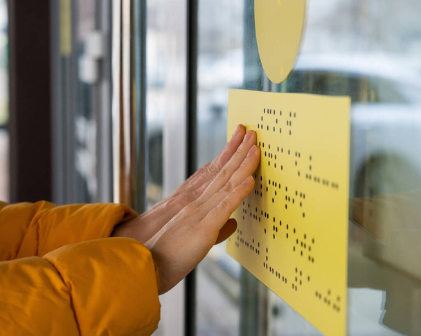Close-up of a woman reading a braille lettering on a glass door - Foto, Imagem