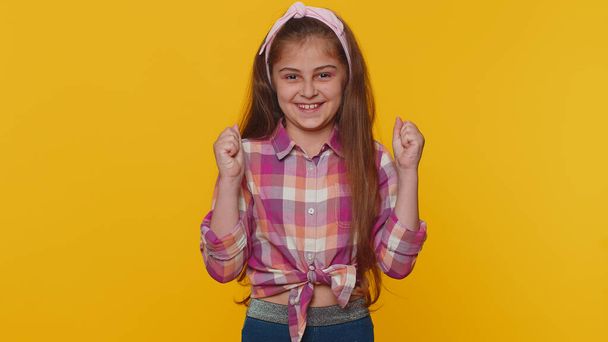 Young preteen child girl kid shouting, raising fists in gesture I did it, celebrating success, winning, birthday, lottery goal achievemen. Little toddler children isolated on studio yellow background - Photo, Image
