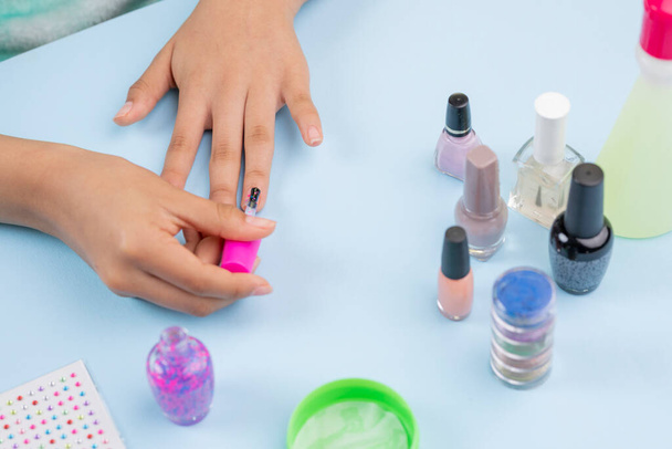 ręce dziewczyny malującej paznokcie lakierem, na niebieskim stole. - Zdjęcie, obraz