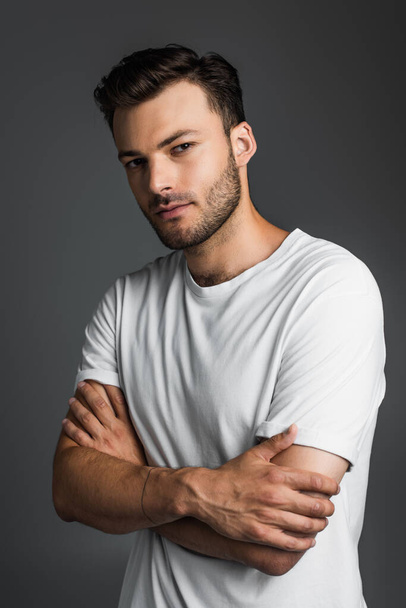 Young brunette man in t-shirt crossing arms isolated on grey  - Foto, Imagem