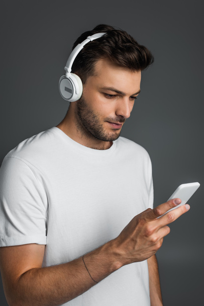 Bearded man using smartphone and headphones isolated on grey  - Foto, imagen
