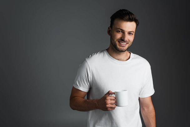 Cheerful man in white t-shirt holding cup of coffee isolated on grey  - Foto, immagini