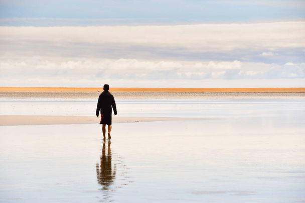 Boy dressed in black with reflection on the water walking to the beach with orange sand - Fjord in the north of Iceland Europe - Φωτογραφία, εικόνα