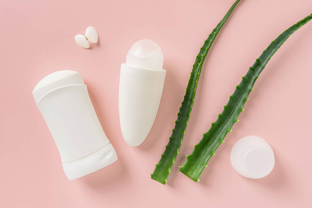 Roll on antiperspirant, solid deodorant and two fresh green aloe leaves over pastel coral background. Natural toiletries for body care. Organic cosmetics for personal hygiene. Top view.  - Foto, Imagen