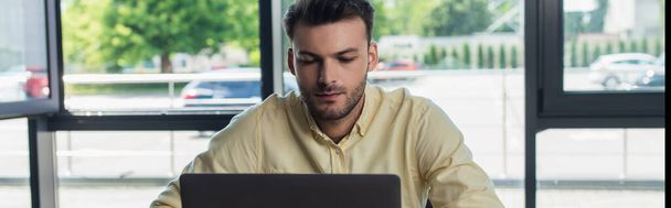 Young businessman using laptop while working in office, banner  - Foto, Imagen