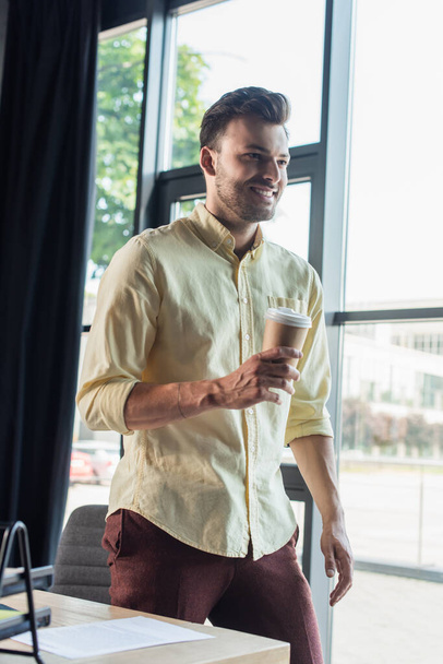 Cheerful businessman in shirt holding takeaway drink in office  - Fotoğraf, Görsel