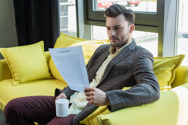 Businessman holding contract and cup on couch in office  - Foto, immagini